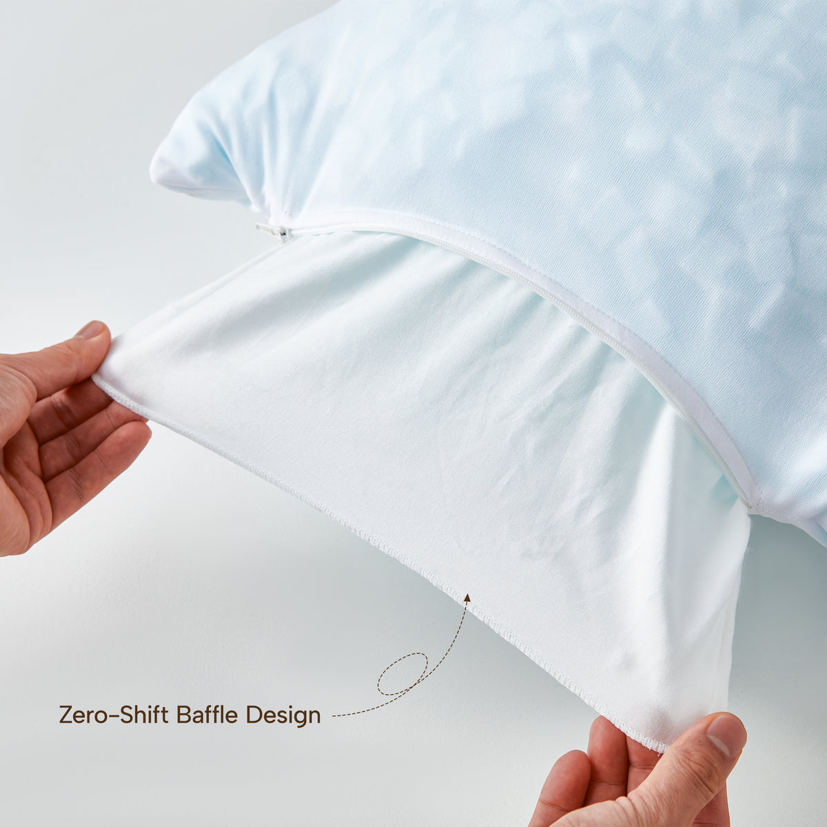 Close-up of a light blue pillow with a white inner baffle layer being pulled open by two hands, with the text 'Zero-Shift Baffle Design' shown on a clean white background.